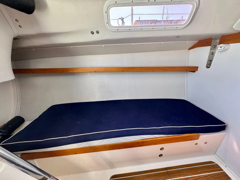 Slide: The Image of 2005 J Boats J/100 cabin interior with blue cushioned berth and wooden accents. - 23