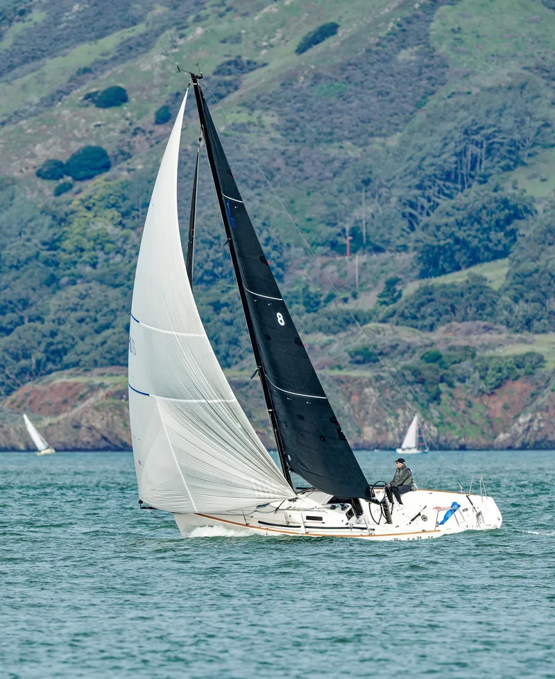 Slide: The Image of 2005 J Boats J/100 sailing near a lush, hilly coastline. - 6