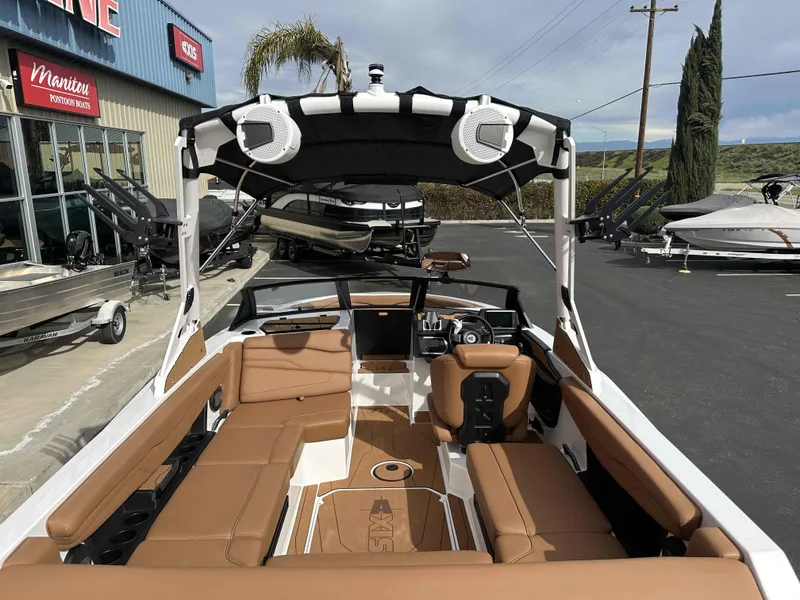Slide: The Image of 2025 Axis T220 boat with tan seating, black canopy, and modern dashboard, parked at a marina. - 12