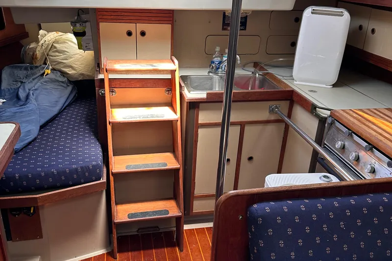 Slide: The Image of 1987 C&C 34 sailboat interior with wooden steps, compact kitchen, and cozy sleeping area. - 11