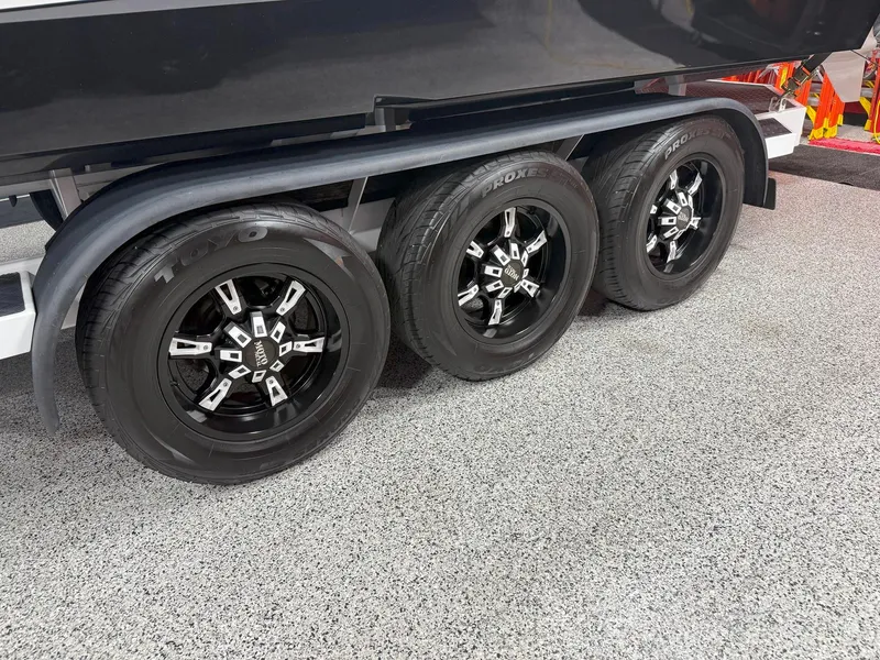Slide: The Image of 2016 Daves Custom Boats M31 trailer with triple black wheels on a speckled floor. - 18