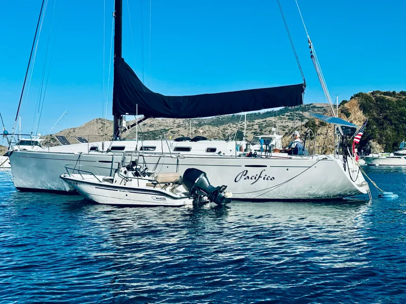 Slide: The Image of 2005 Beneteau First 44.7 sailboat anchored in scenic bay with small motorboat nearby. - 2