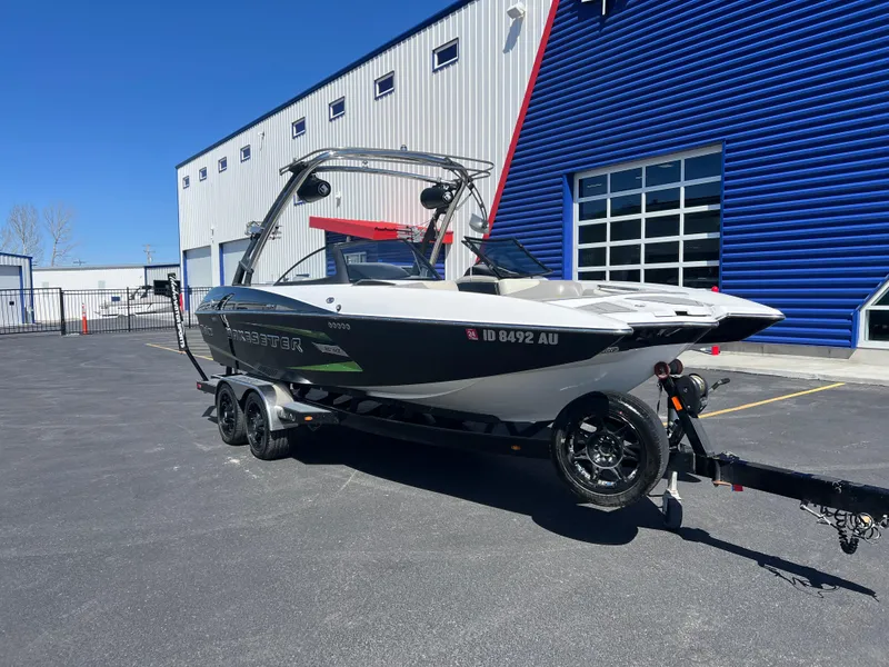 Slide: The Image of 2014 Malibu W22MXZ boat on trailer, parked outside a blue and white building. - 3
