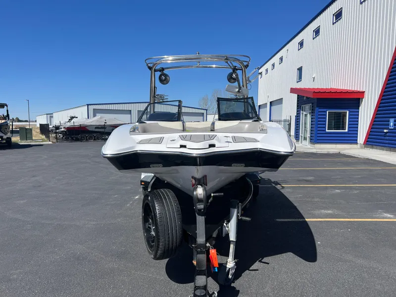 Slide: The Image of 2014 Malibu W22MXZ boat on trailer, parked outside a modern building. - 4