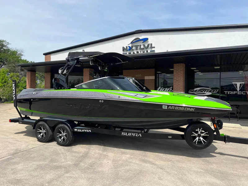 Slide: The Image of 2014 Supra SA450 boat with green and black design on a trailer outside dealership. - 1