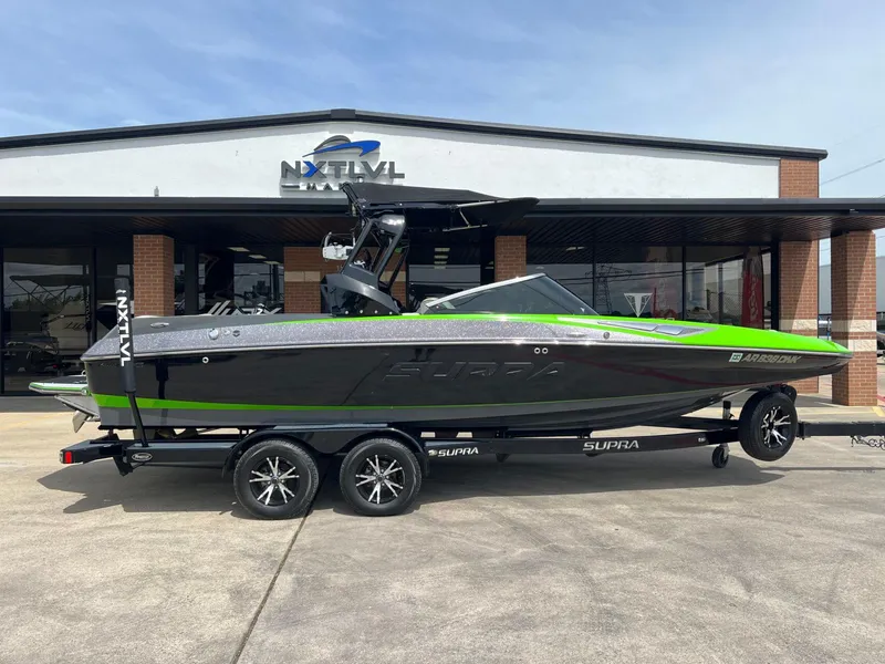 Slide: The Image of 2014 Supra SA450 boat with green accents on a trailer outside a dealership. - 2