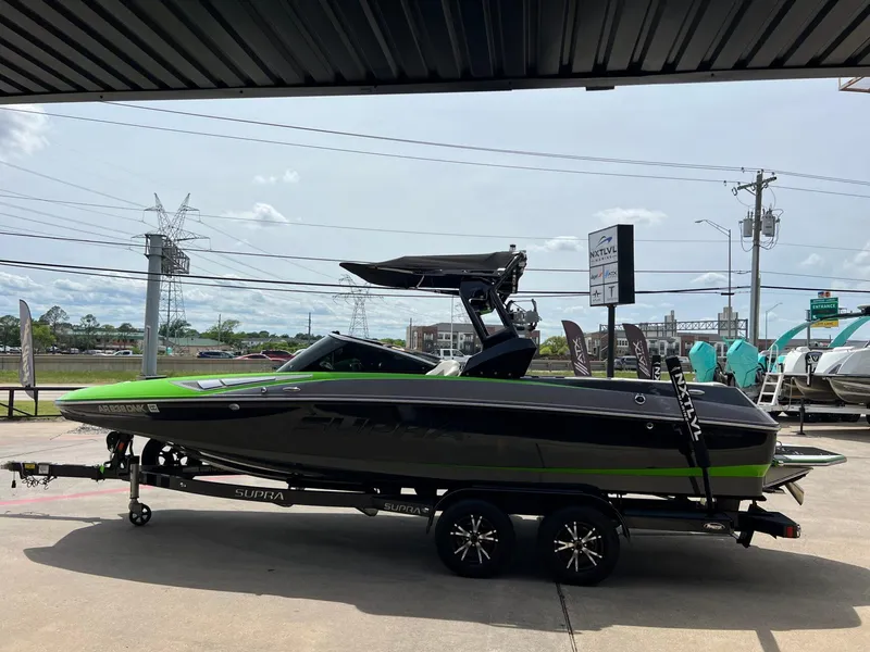 Slide: The Image of 2014 Supra SA450 boat with green and black design on a trailer in a parking lot. - 23