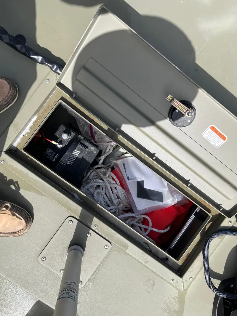 Slide: The Image of Open storage compartment in 2022 Tracker Grizzly 1648 SC boat, containing battery and ropes. - 10