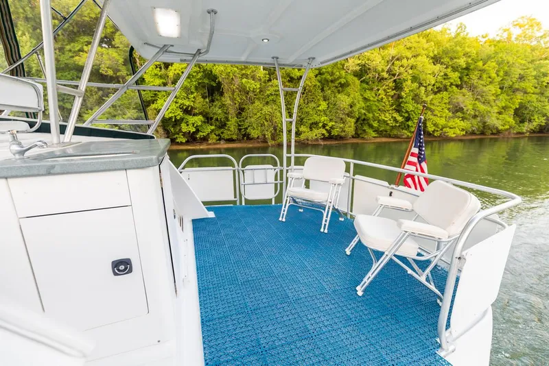 Slide: The Image of 1996 Mainship 37 Aft Cabin boat deck with chairs, blue carpet, and American flag by a river. - 13