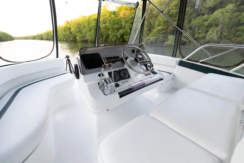Slide: The Image of 1996 Mainship 37 Aft Cabin helm with white seating, steering wheel, and river view. - 7