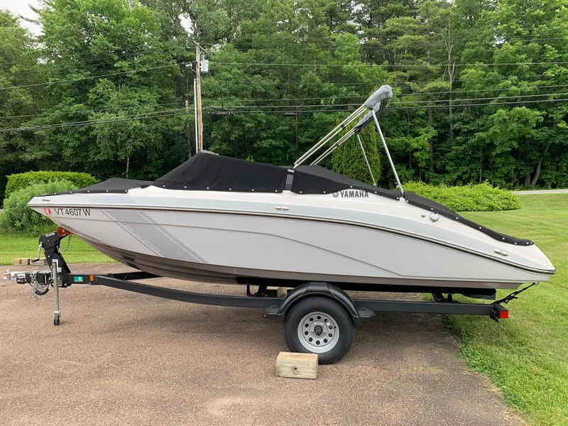 Slide: The Image of 2023 Yamaha SX195 boat on trailer, parked outdoors with lush green background. - 13