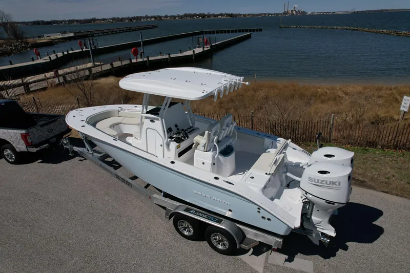 Slide: The Image of 2025 Cape Horn 24 XS boat on trailer by waterfront, featuring Suzuki outboard motor. - 2