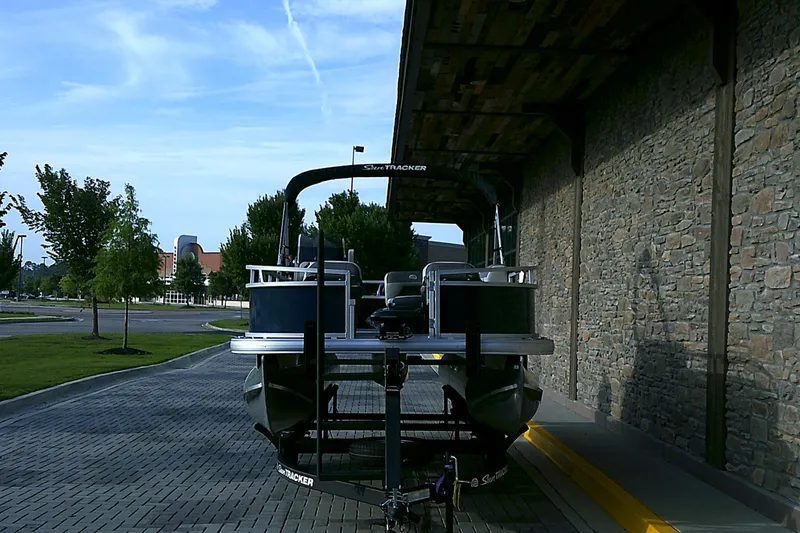 Slide: The Image of 2025 Sun Tracker Bass Buggy 16 XL Select pontoon boat parked on a paved driveway. - 2