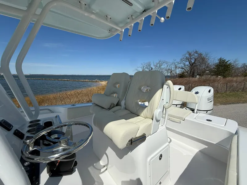 Slide: The Image of 2025 Cape Horn 24 XS boat interior with plush seating and steering wheel, near a scenic waterfront. - 24