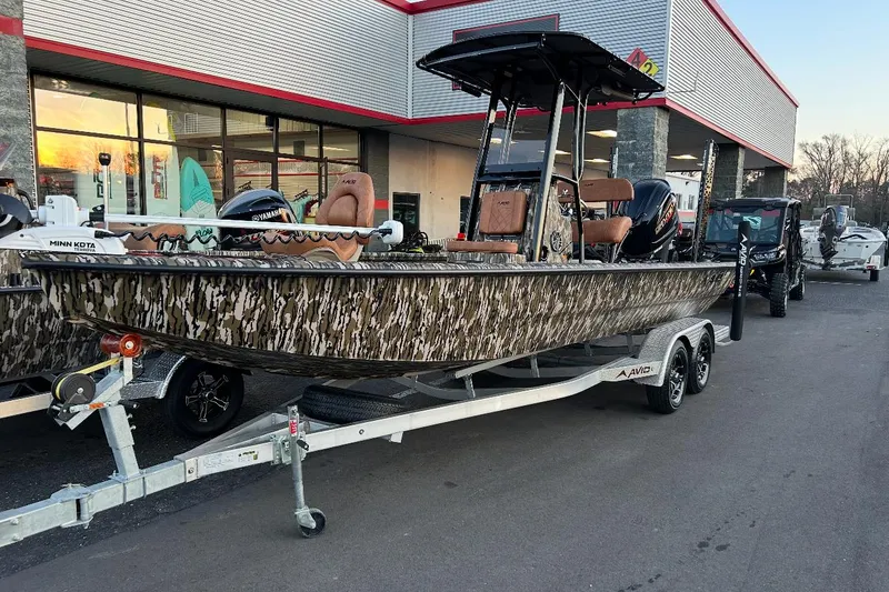 Slide: The Image of 2024 Avid 23 Mag boat with camouflage design on a trailer outside a dealership. - 6