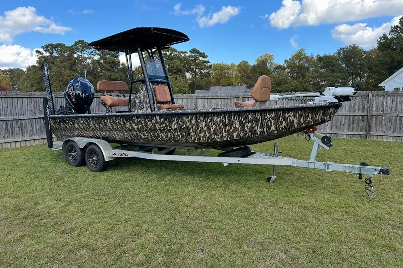 Slide: The Image of 2024 Avid 23 Mag boat on trailer, camo design, parked on grass with trees in background. - 7