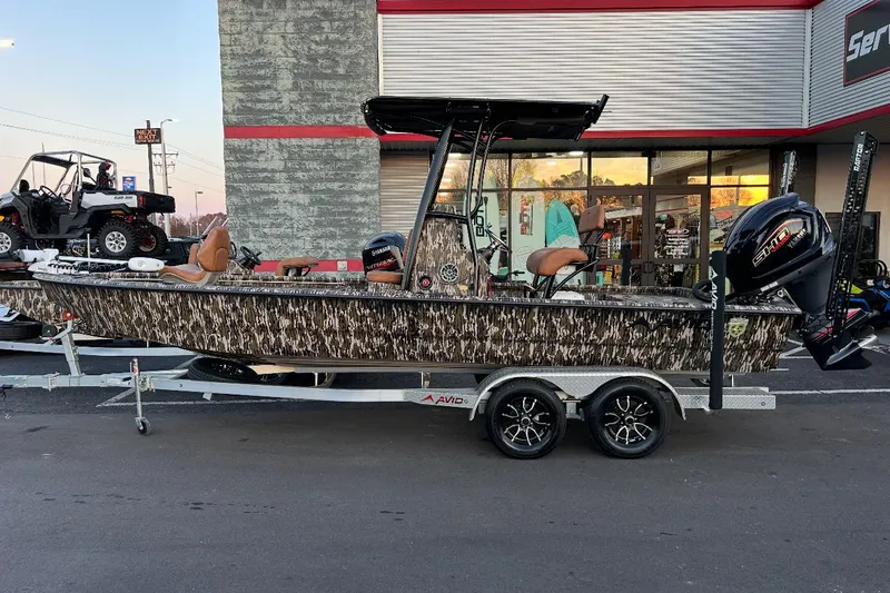 Slide: The Image of 2024 Avid 23 Mag boat on trailer, camo design, parked outside dealership. - 8