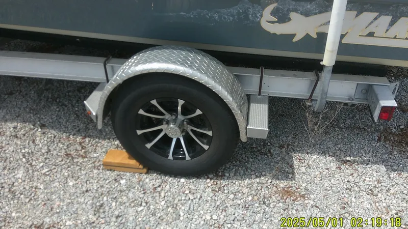 Slide: The Image of Trailer wheel of a 2023 Mako 18 LTS boat on gravel, secured with a chock. - 15