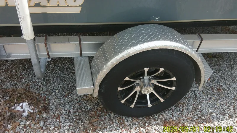 Slide: The Image of 2023 Mako 18 LTS trailer wheel with diamond plate fender on gravel. - 18