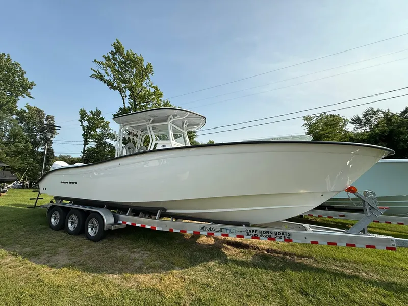 Slide: The Image of 2025 Cape Horn 32 XS boat on trailer, parked on grass, under clear sky. - 2