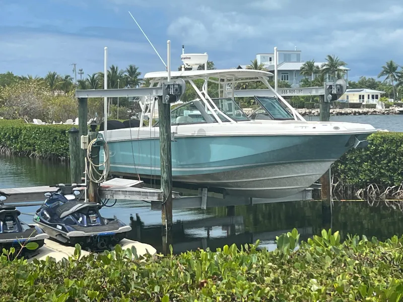 Slide: The Image of 2013 Boston Whaler 270 Vantage boat on lift, with jet skis nearby, tropical setting. - 33
