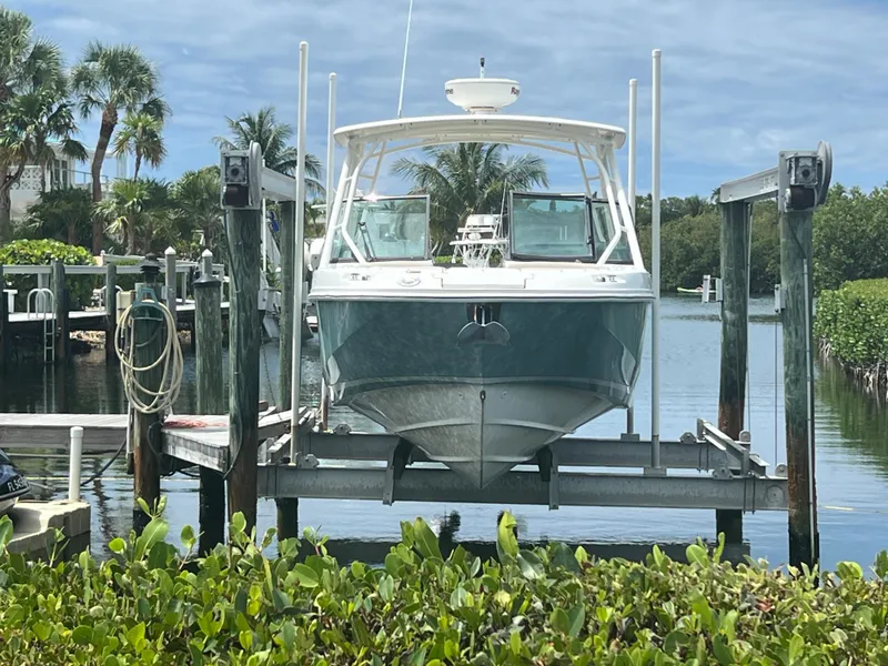 Slide: The Image of 2013 Boston Whaler 270 Vantage boat on lift, surrounded by lush greenery and calm water. - 6