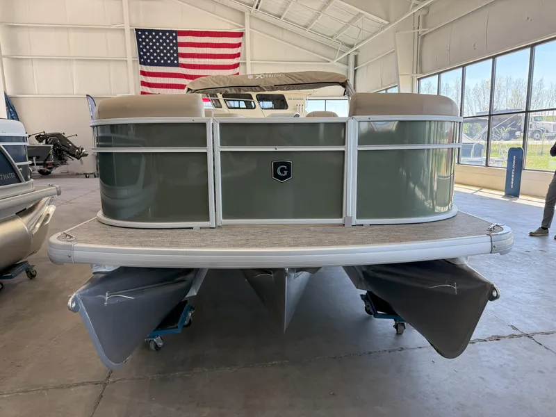 Slide: The Image of 2025 Godfrey EX2086SFLX Tritoon boat in showroom with American flag backdrop. - 2