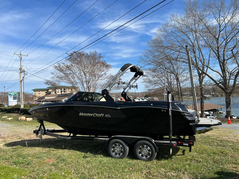 Slide: The Image of 2020 MasterCraft NXT22 boat on trailer, parked near a lake with clear blue sky. - 1