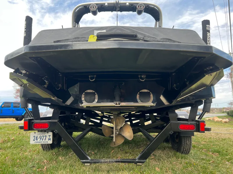 Slide: The Image of 2020 MasterCraft NXT22 boat rear view, showcasing propeller and trailer on grass. - 21
