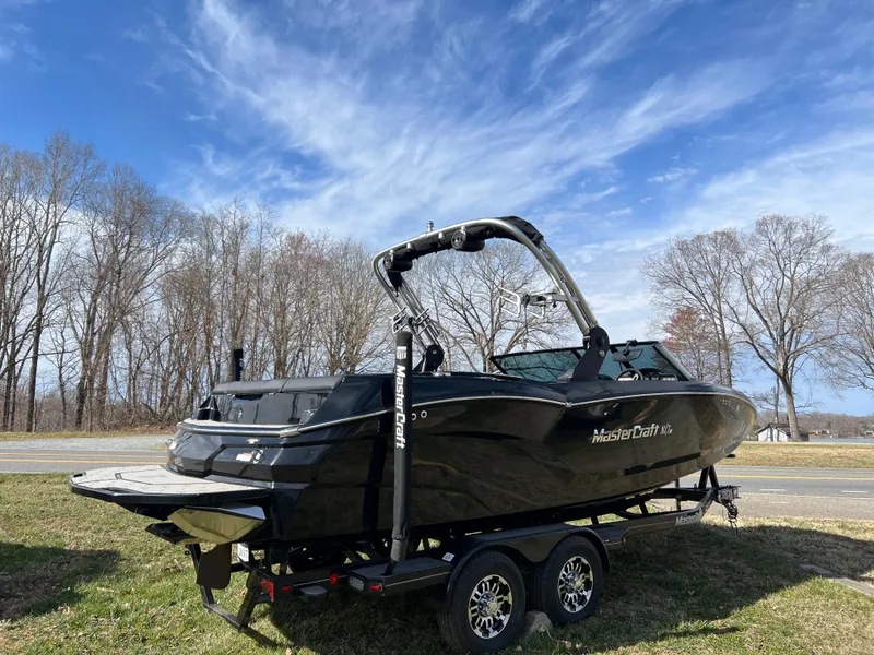 Slide: The Image of 2020 MasterCraft NXT22 boat on trailer, parked outdoors under a clear blue sky. - 4