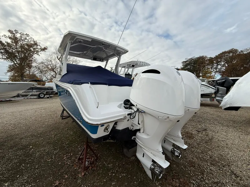 Slide: The Image of 2018 Edgewater 262 CX boat with dual outboard engines, parked on gravel. - 2