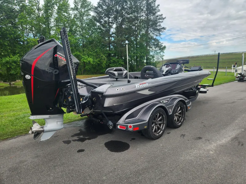 Slide: The Image of 2021 Triton 20 TRX boat on trailer, parked on a road with green trees in the background. - 2