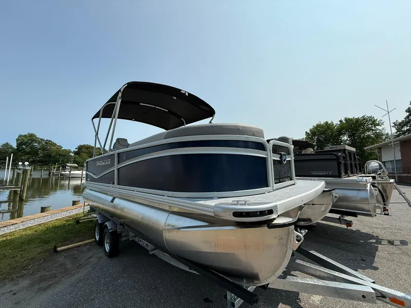 The Image of 2025 Premier 200 Sunscape RE XLC pontoon boat on trailer, parked near a waterfront. - 1