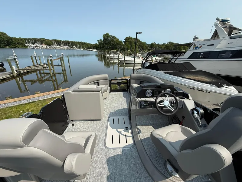 Slide: The Image of 2025 Premier 210 Sunsation RL pontoon boat interior at marina, featuring plush seating and steering console. - 5