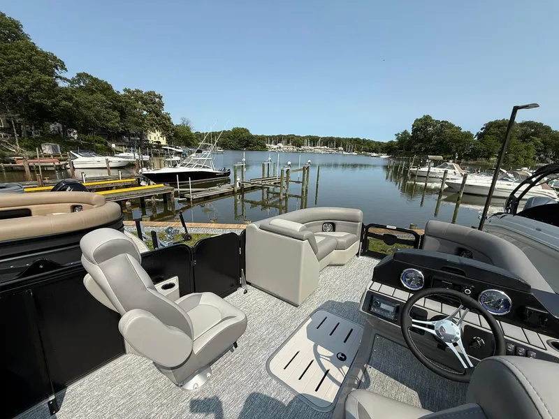 Slide: The Image of 2025 Premier 210 Sunsation RL pontoon boat docked by a scenic lake with lush surroundings. - 6