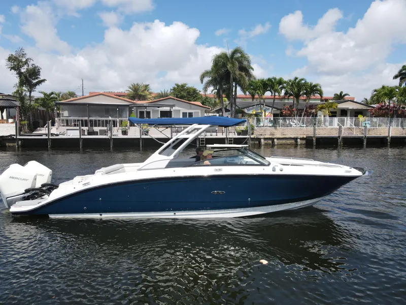 The Image of 2021 Sea Ray SDX 290 Outboard boat cruising on a sunny day near waterfront homes. - 0