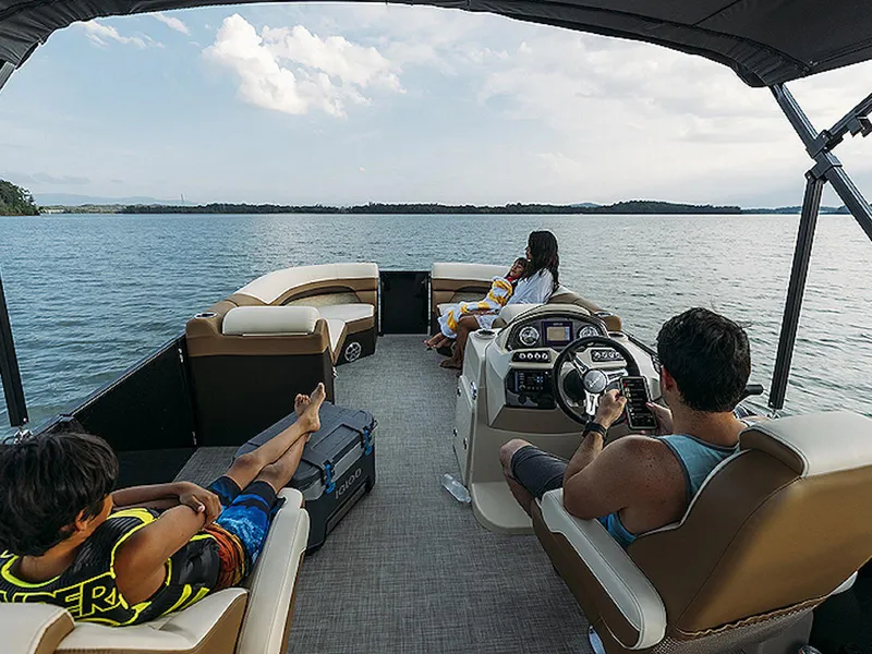 Slide: The Image of 2024 Lowe L-Shaped SS 210 pontoon boat on a serene lake with passengers relaxing. - 9