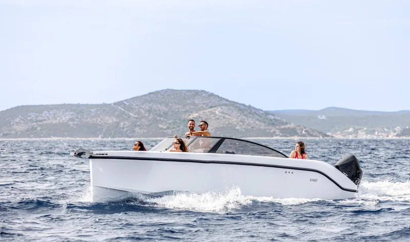 Slide: The Image of 2025 Rand Supreme 27 boat cruising on open water with passengers, scenic hills in background. - 16