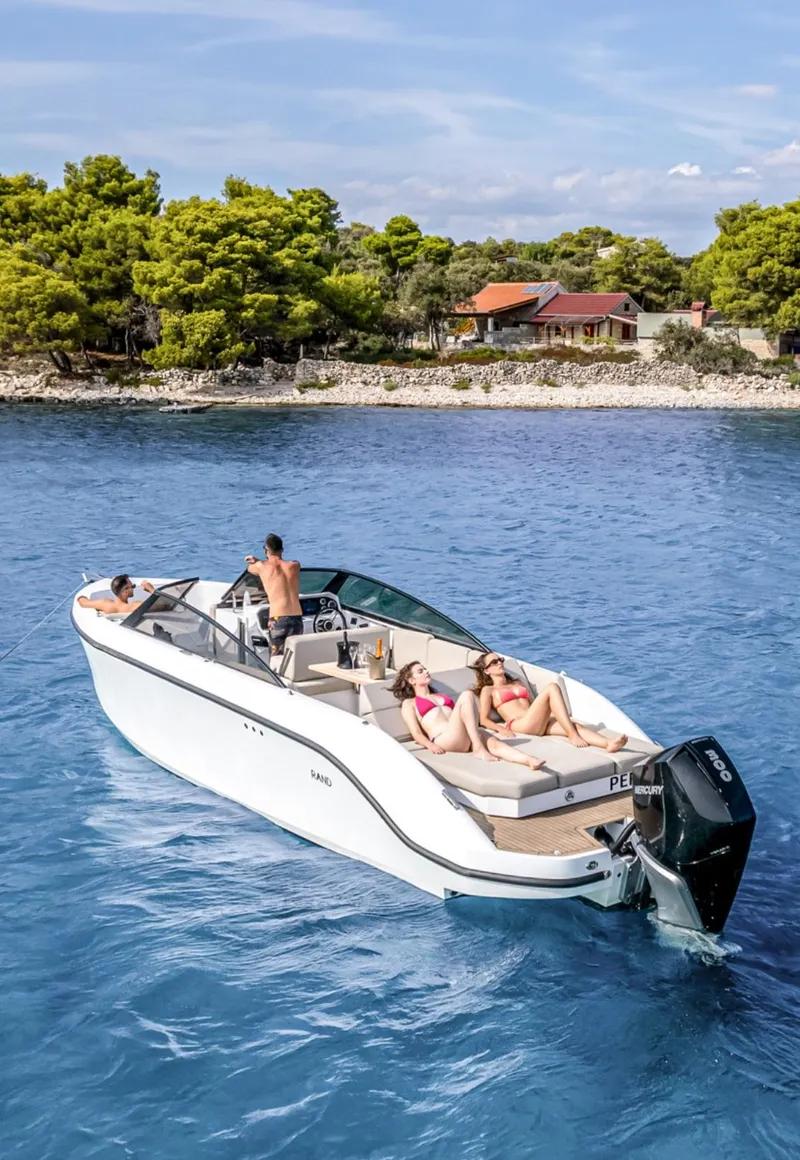 Slide: The Image of 2025 Rand Supreme 27 boat cruising near a scenic shoreline with passengers relaxing onboard. - 27