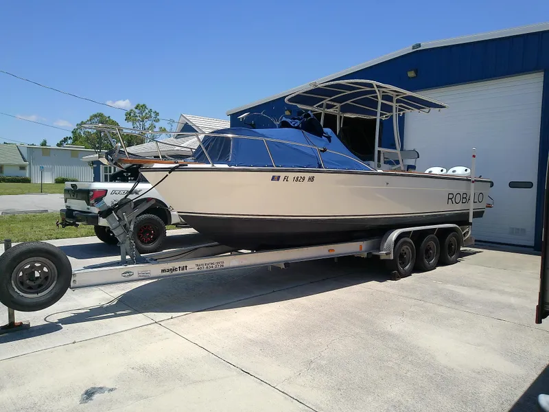 Slide: The Image of 1985 Robalo 2520 Center Console boat on trailer, parked outside a blue building. - 2