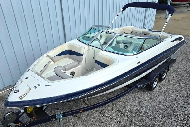 Slide: The Image of 2008 Bryant 246 BR boat with trailer, white and blue, parked near a building. - 1