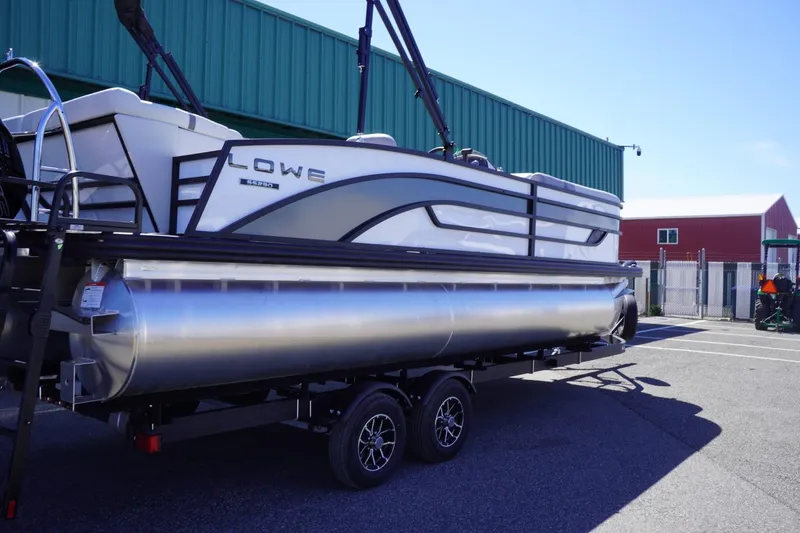 Slide: The Image of 2025 Lowe SS 230 pontoon boat on trailer, parked outdoors near industrial buildings. - 12