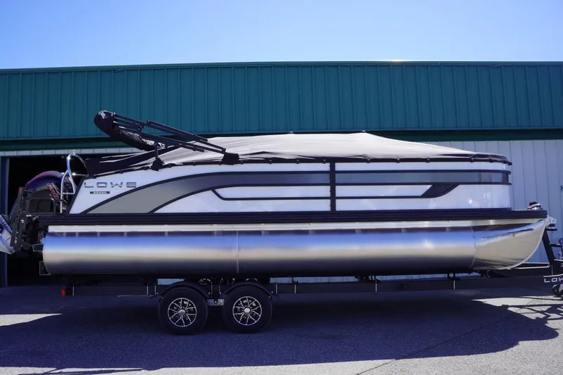 Slide: The Image of 2025 Lowe SS 230 pontoon boat on trailer, covered, parked outdoors. - 2