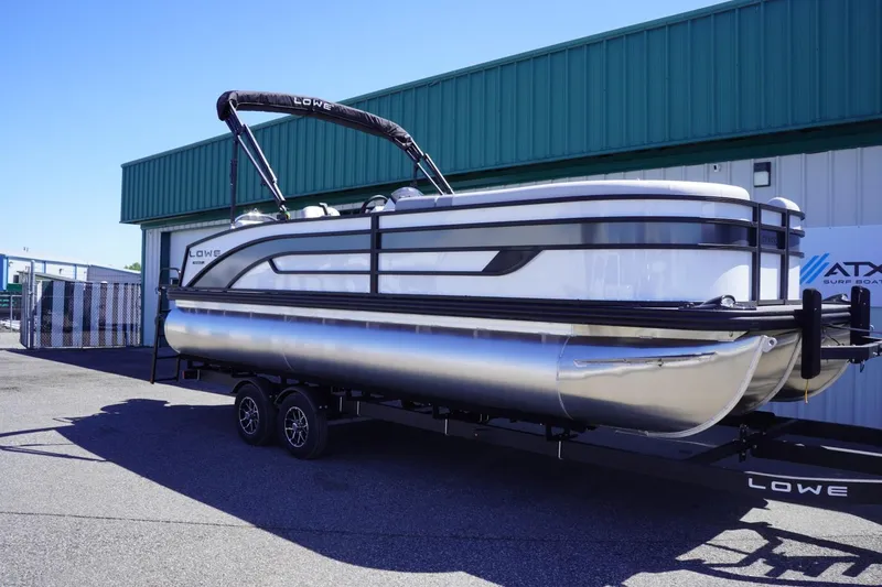 Slide: The Image of 2025 Lowe SS 230 pontoon boat on trailer, parked outside a green building. - 3