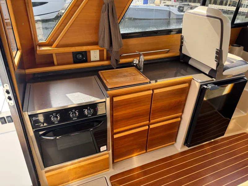 Slide: The Image of 2014 Cutwater C-28 Coupe interior kitchen with wood cabinetry, stove, and sink. - 17