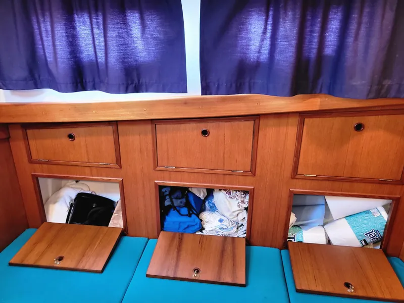 Slide: The Image of Wooden storage compartments inside a 1978 Fisher 25 boat, with blue cushions and curtains. - 17