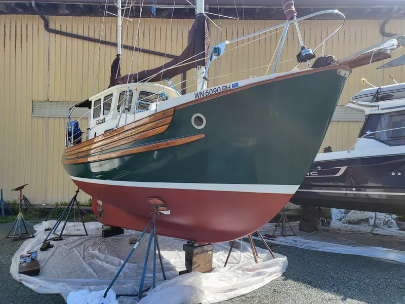 Slide: The Image of 1978 Fisher 25 sailboat on stands, green hull, wooden accents, in a boatyard. - 35