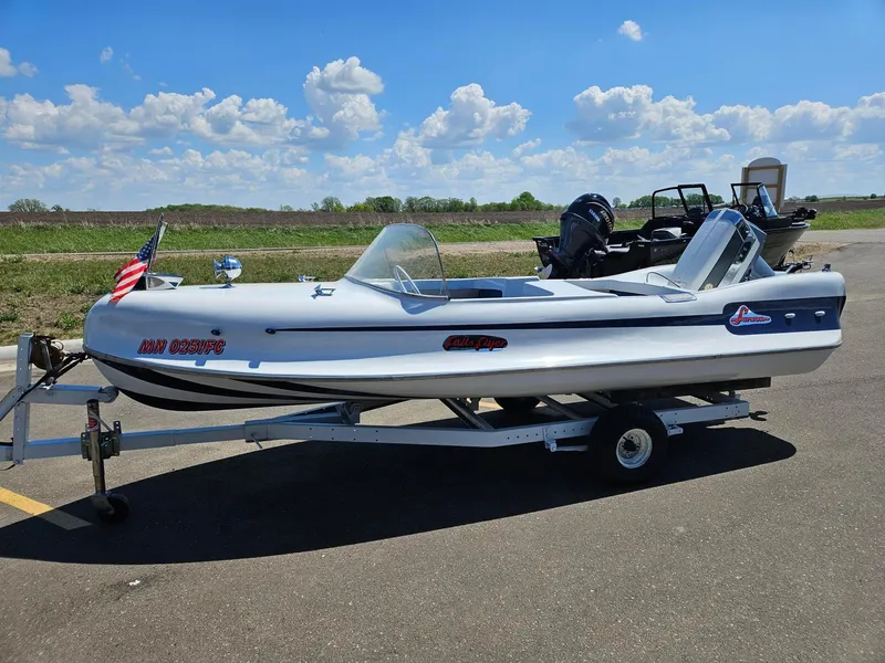 The Image of 1958 Larson Falls Flyer boat on trailer, parked outdoors under a blue sky. - 1