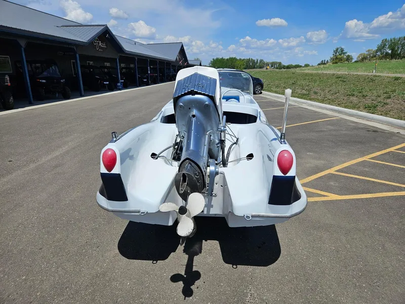 Slide: The Image of 1958 Larson Falls Flyer boat with outboard motor, parked outdoors under a clear blue sky. - 3