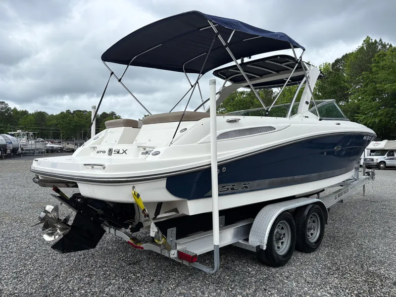 Slide: The Image of 2011 Sea Ray 270 SLX boat on trailer, blue and white, with canopy, parked on gravel. - 5